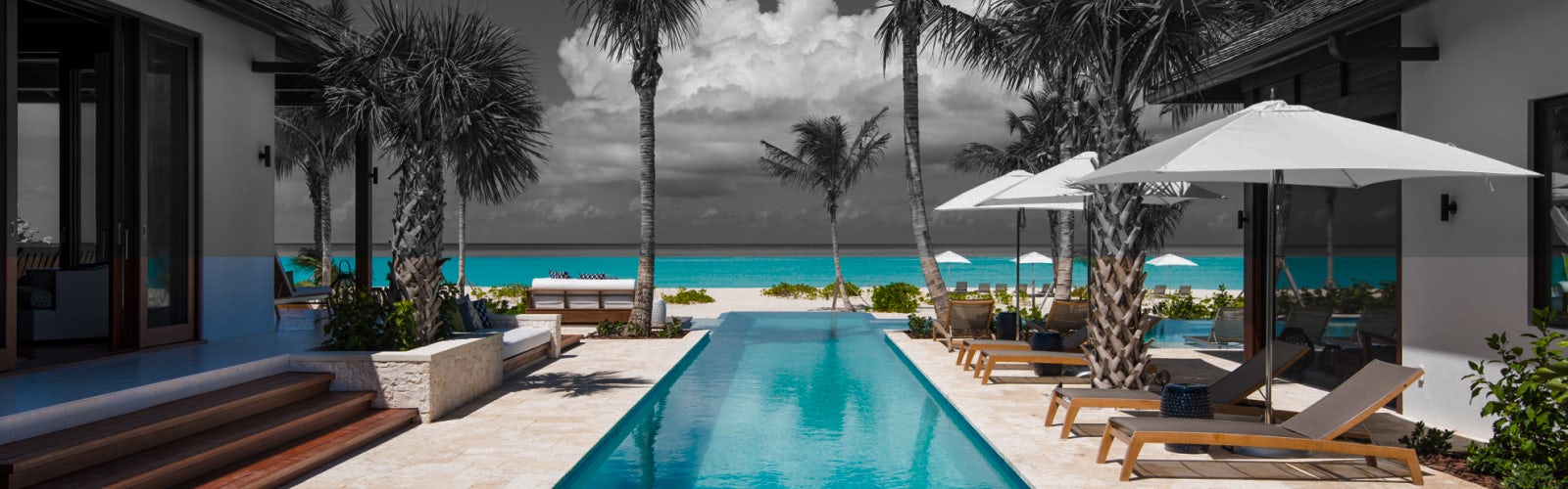 A desaturated image of a luxury villa with pops of blue color on the swimming pool and ocean behind