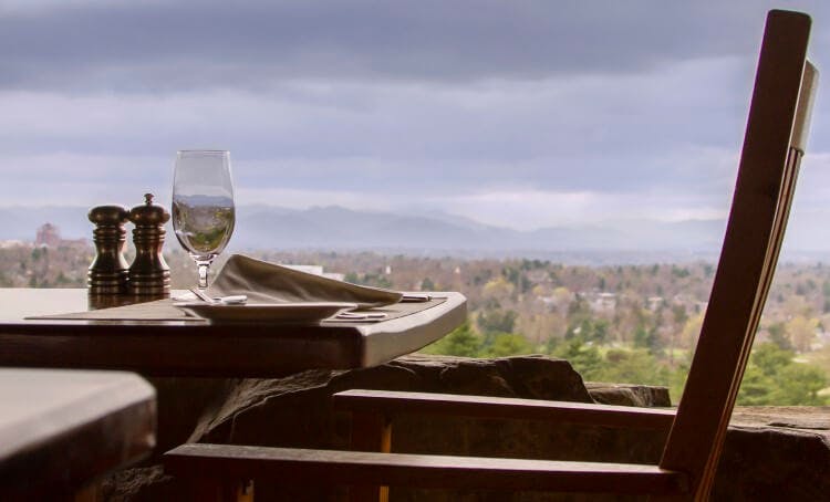 A restaurant table set with wine glasses, a plate and salt and pepper mills, next to a window with a mountain view