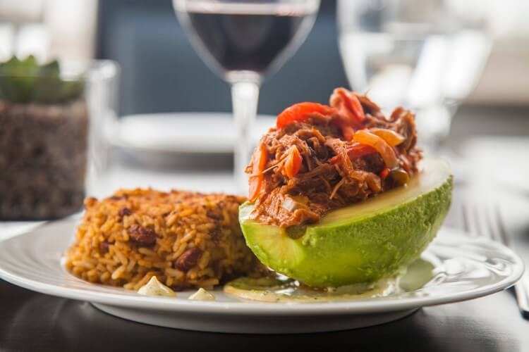 A traditional Caribbean dish of pulled meat served inside and avocado with rice and beans on the side