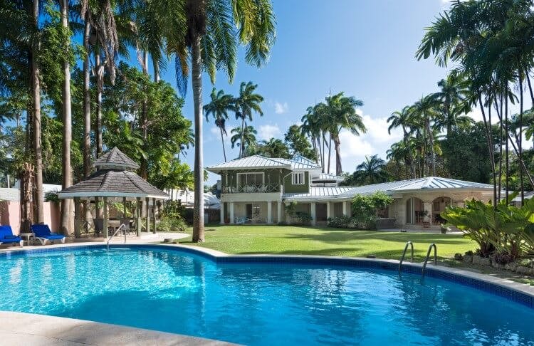 large pool surrounded by a villa, lawn and palm trees