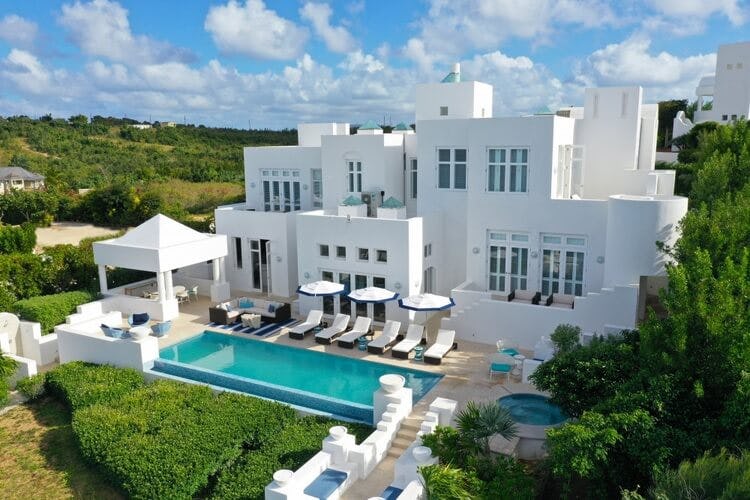 large white villa and pool surrounded by greenery