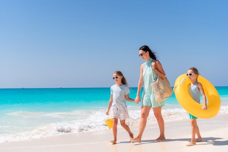 A woman and two girls walk along a white sand beach