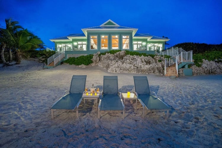 green villa at dusk in background with loungers on beach