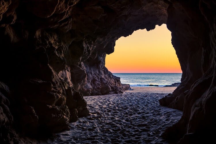 view of beach at sunset through a cave