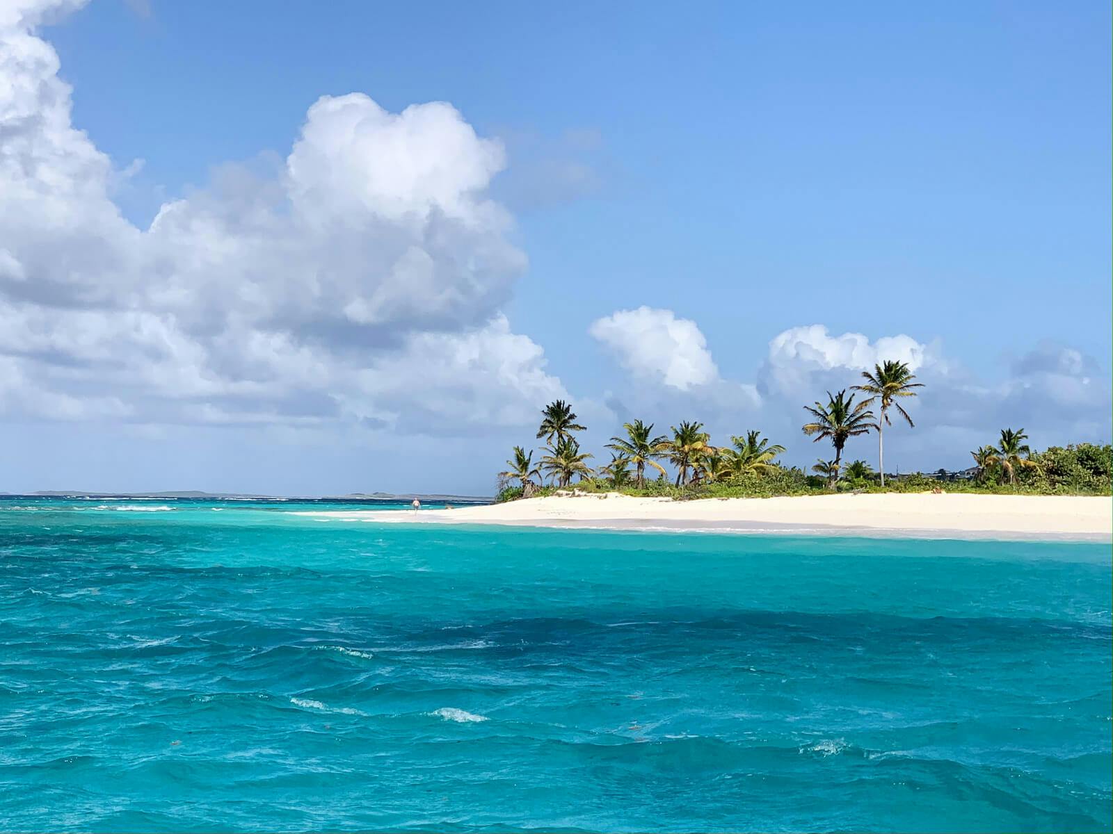 Anguilla island from the ocean, with a spit of white sand topped with palm trees