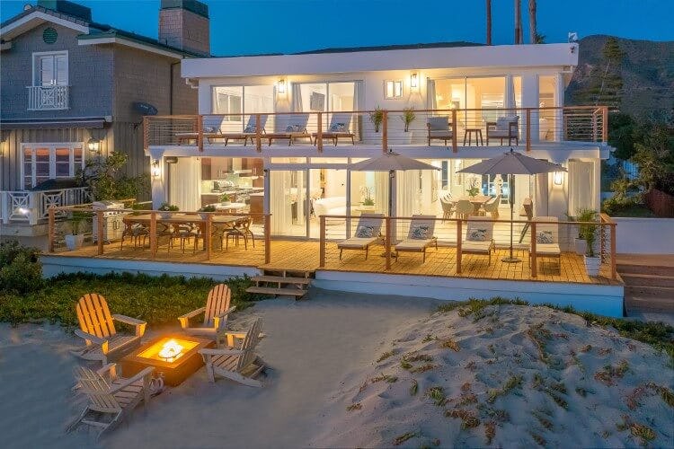 lit up white villa at dusk on a beach with a firepit