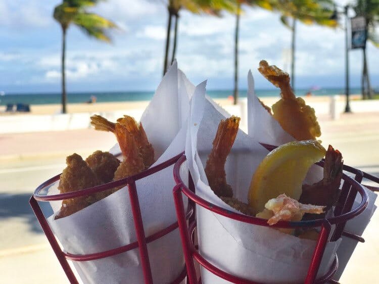 Cones of friend prawns and chips with a Florida beach in the background