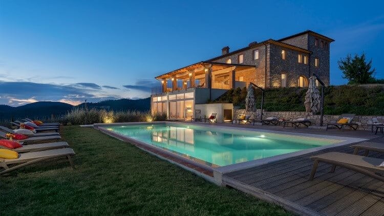 grand rustic villa with lit up pool at dusk