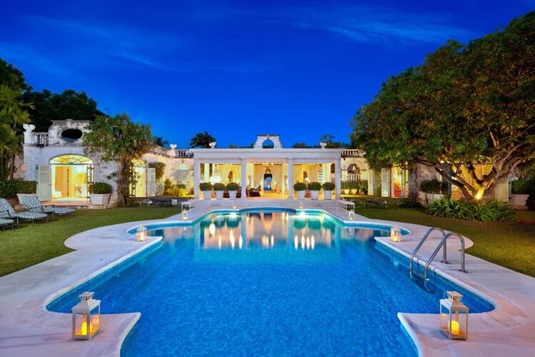 sprawling white mansion with pool and lanterns at dusk