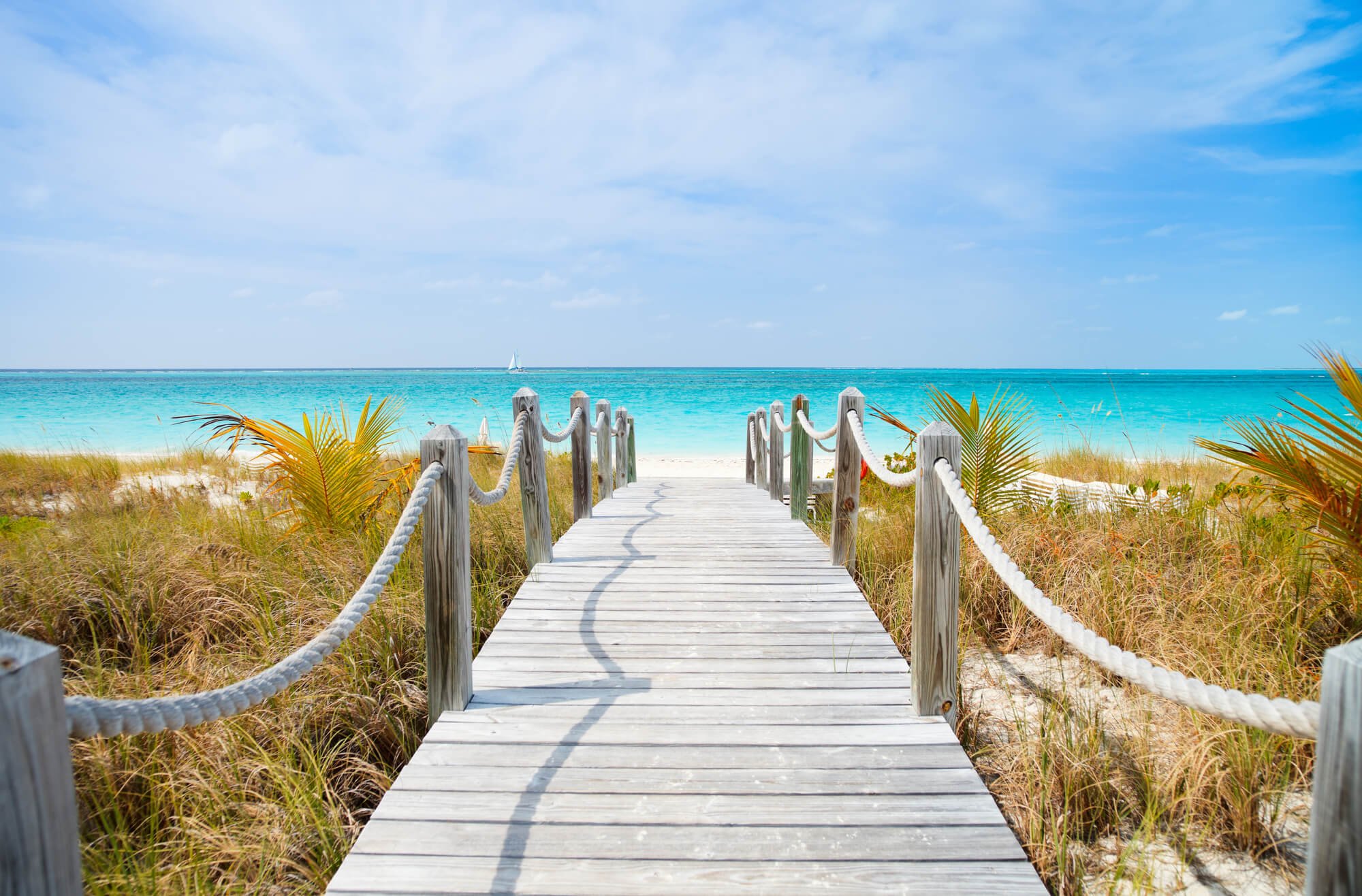 Wooden boardwalk leading towards and white sand beach and sea