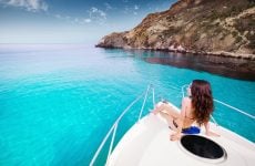 A person in a swimsuit relaxes on the bow of a yacht in clear blue water