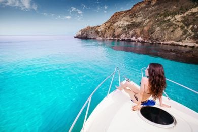 A person in a swimsuit relaxes on the bow of a yacht in clear blue water