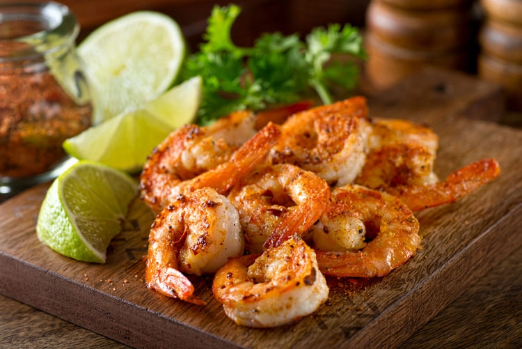 Shelled prawns on a wooden board with seasoning and lime wedges