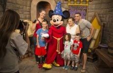 A family gathered around a person dressed as Wizard Mickey Mouse having their photo taken