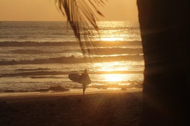 Best resorts in Bali - person carrying a surfboard to the sea at sunset