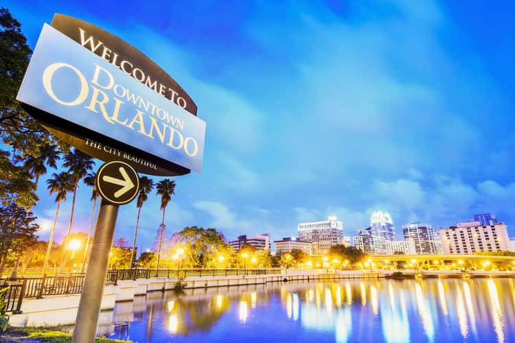 a sign saying 'Welcome to Downtown Orlando' with a city in the background