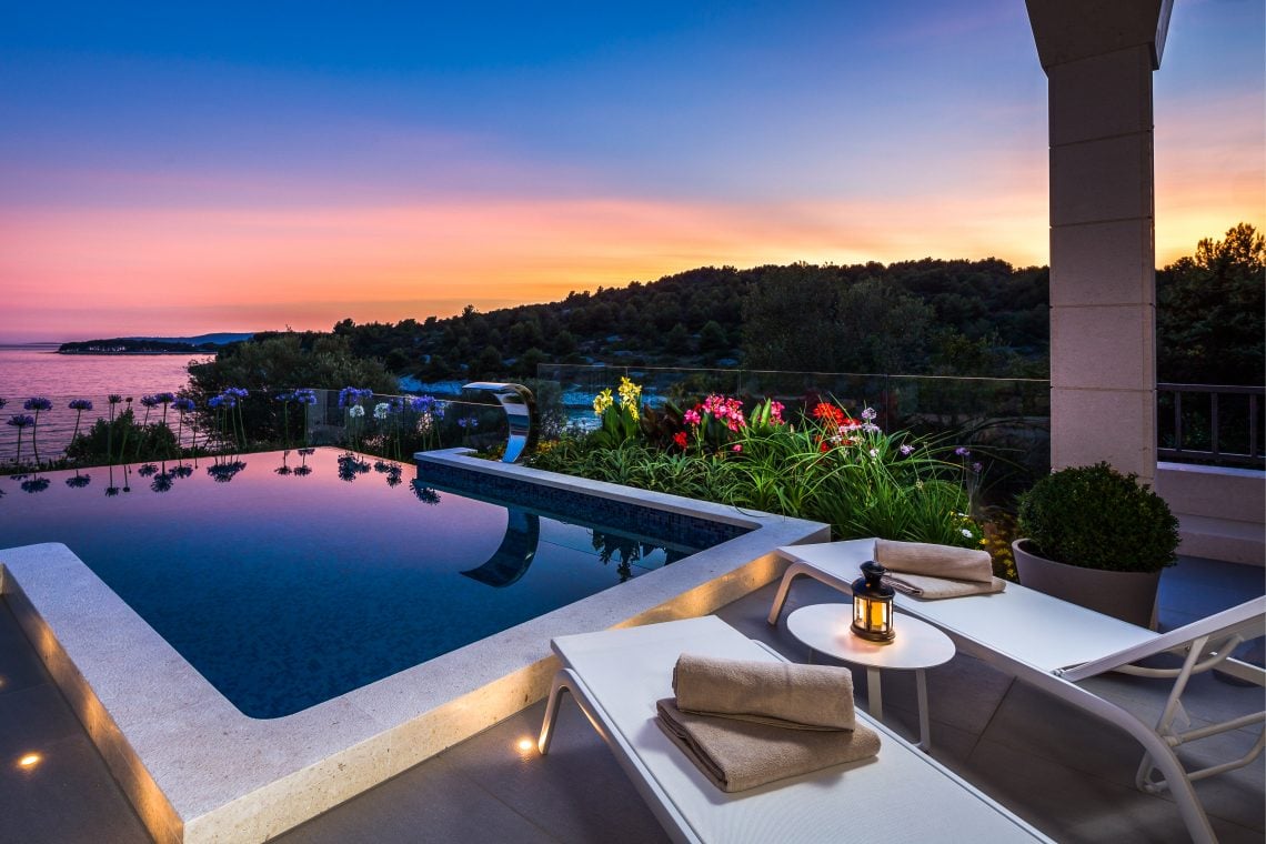A luxury villa with infinity pool and loungers overlooking the sea at sunset