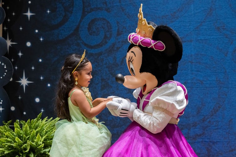 Where to find characters at Disney World - a young girl in a princess dress holding hands with Minnie Mouse
