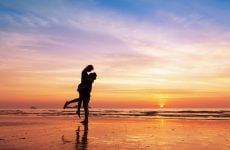 A silhouette of a young couple on a beach at sunset - the man lifting the woman into the air in an embrace