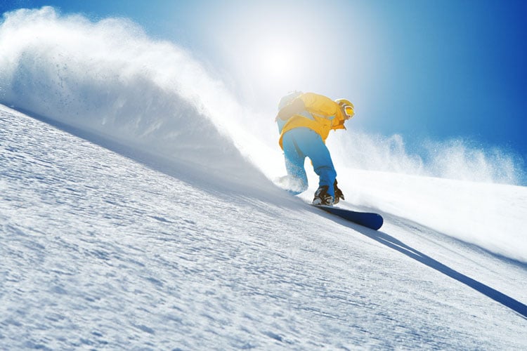 A person in a yellow jacket and blue trousers snowboarding