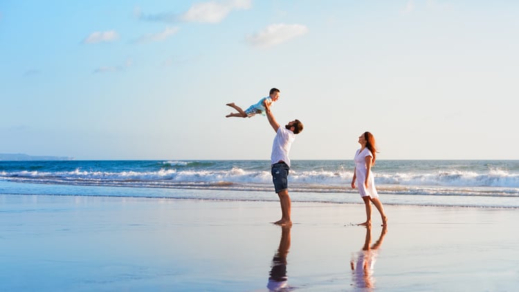 A family with a young child play on a white sand beach