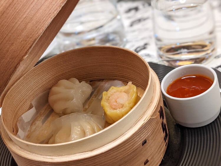 Dim sum dumplings in a traditional steamer with dipping sauce on the side