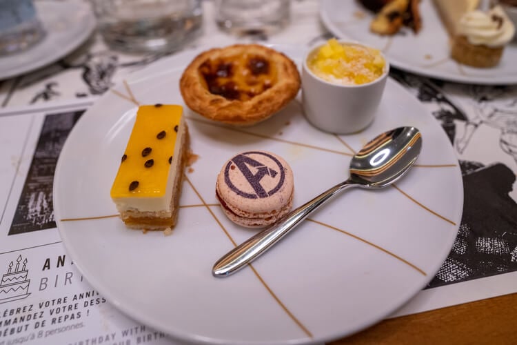 A plate of mini deserts including a Portuguese egg tart, a cheesecake slice, and a macaron
