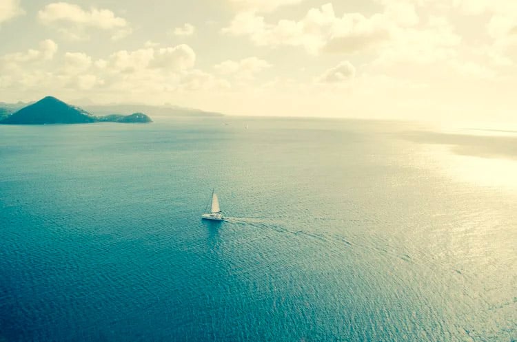 A yacht sailing on a flat sea with a small mountain island in the background
