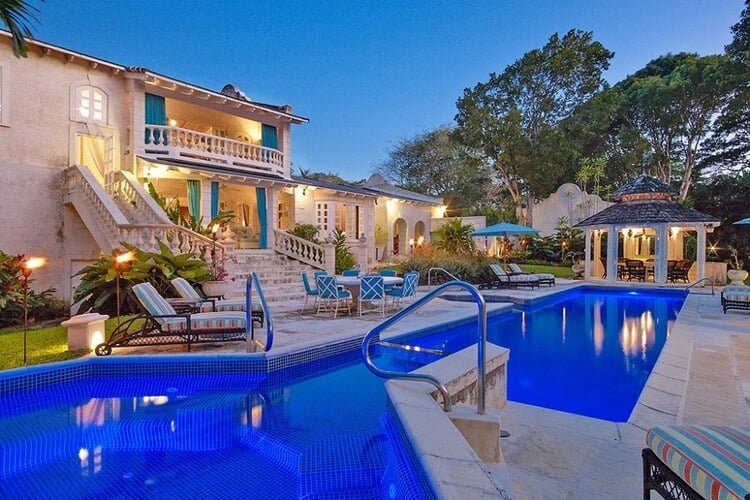 Stone stairs coming out of a large Barbados villa to a swimming pool, with outdoor seating areas and sun loungers.
