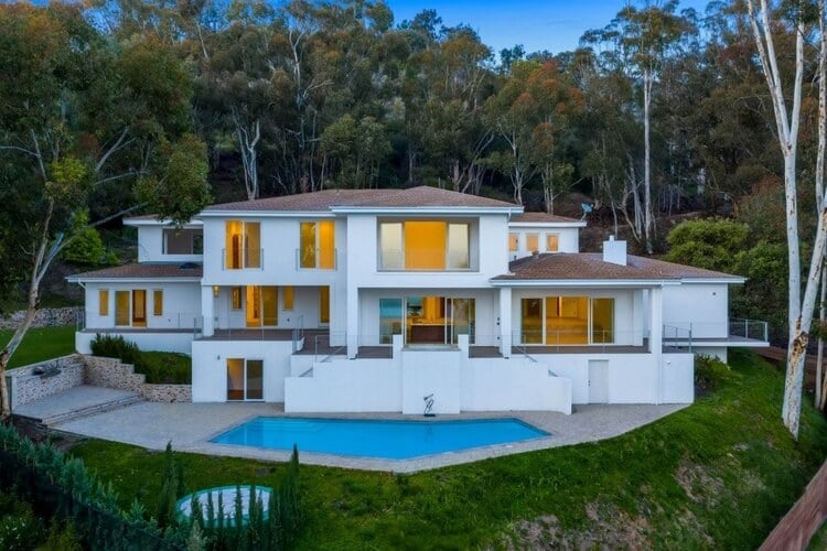 A large white Malibu villa with a private pool, surrounded by trees