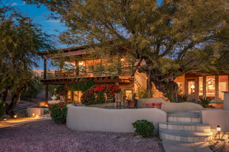 A large 2 story villa with a large tree and seating area outside