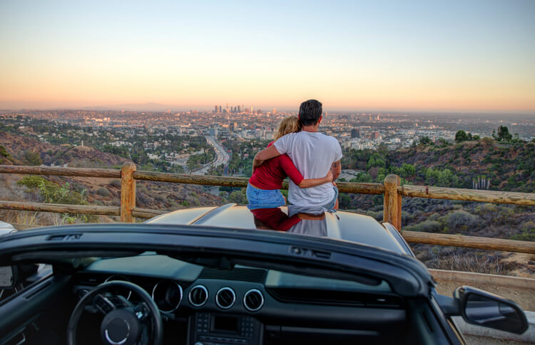 A couple sitting on a car bonnet looking at the Los Angeles skyline