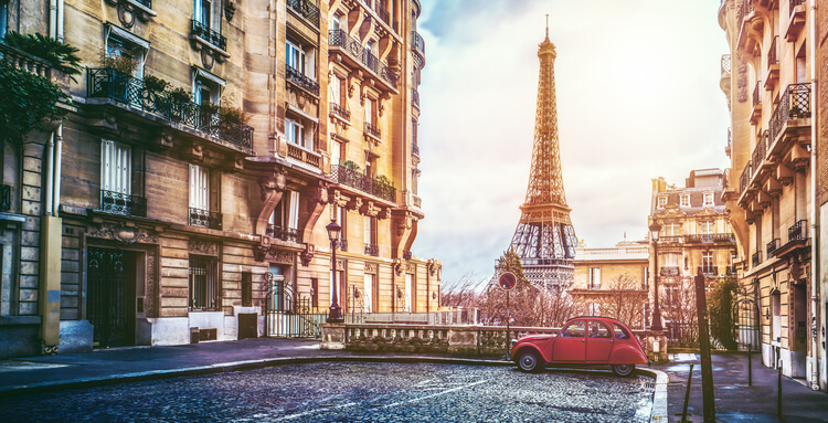 A softly lit street in Paris, with a view of the Eiffel Tower and a VW Beetle car