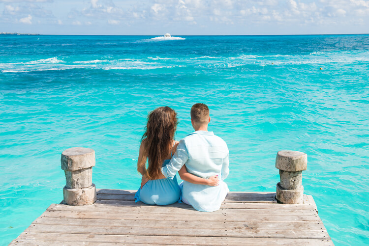 A couple sitting on the edge of a jetty in the Caribbean