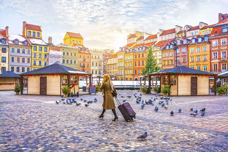 A lady wheeling her luggage through Warsaw Old Town Square in winter