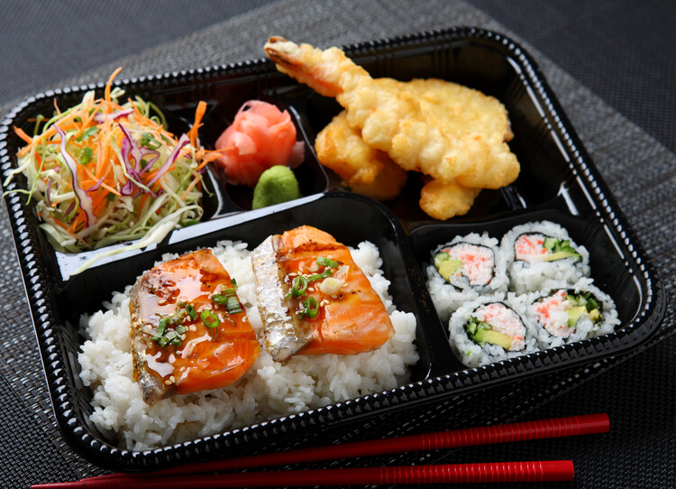 A bento box with tempura prawns, sushi and pickles