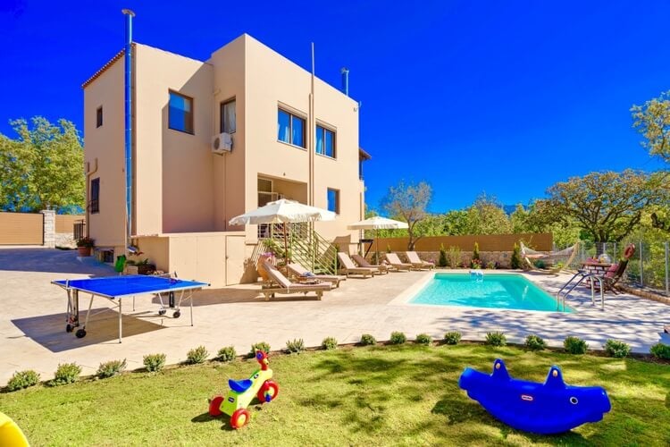 A sandy villa with a pool, and a lawn with children's toys