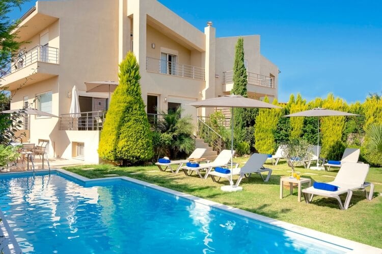 A white villa with several terraces against a blue background, with a pool and several sun loungers in the foreground
