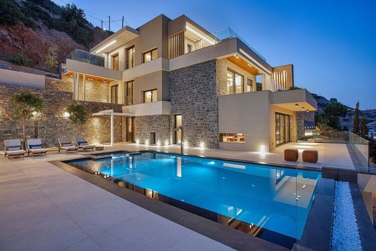 A classy villa at dusk with a large, sophisticated pool in the foreground
