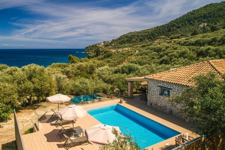 A stone villa with pool, sun loungers, and the sea in the background
