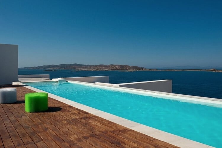 A wooden deck and large infinity pool overlooking the sea and land in the distance