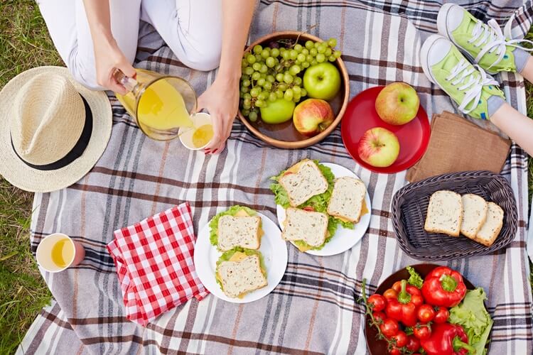 a brightly coloured picnic with juice, fruit and sandwiches