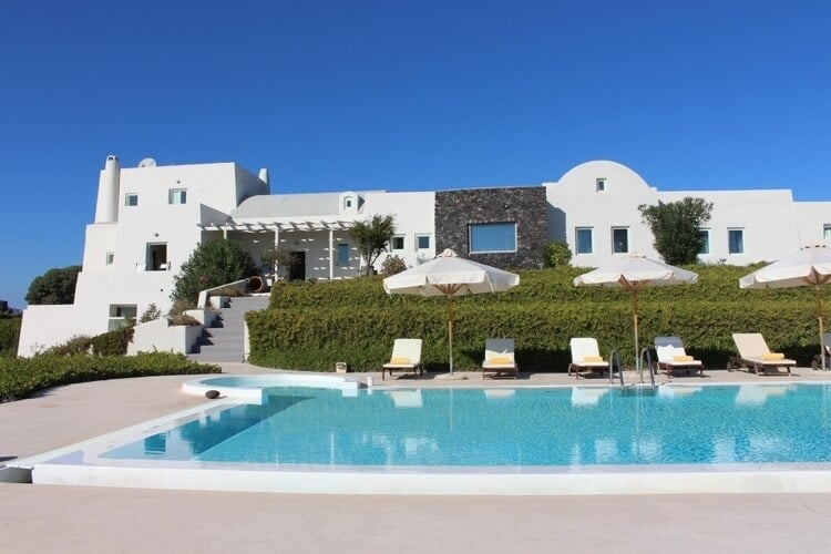 A huge, white villa with expansive shrubbery, five sun loungers and a large pool in the foreground