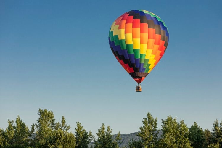 A colorful hot air balloon floating above some trees.