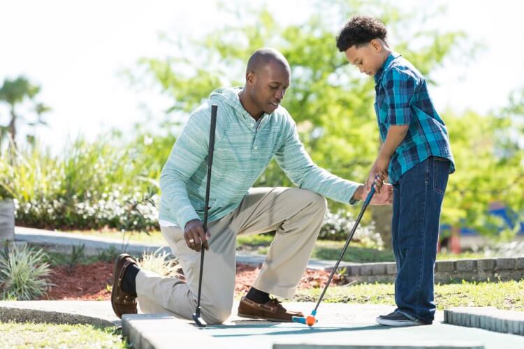 Father teaching his son how to play mini golf.