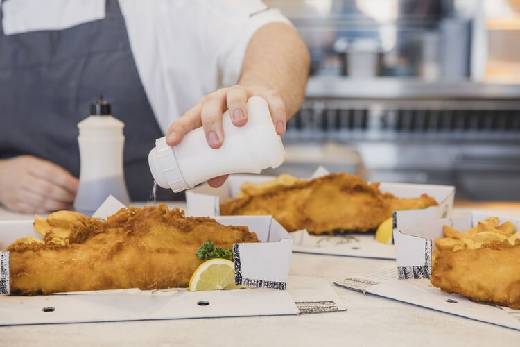 someone pouring salt on fish and chips