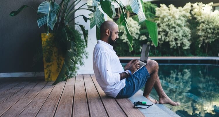 man on laptop next to swimming pool