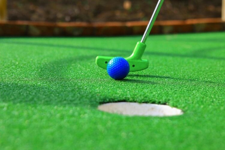 A green golf club putting a blue golf ball into the hole.
