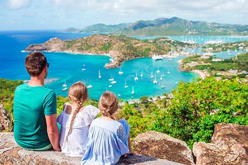 A family of a man and two girls sitting on a rock overlooking English Harbor in Antigua