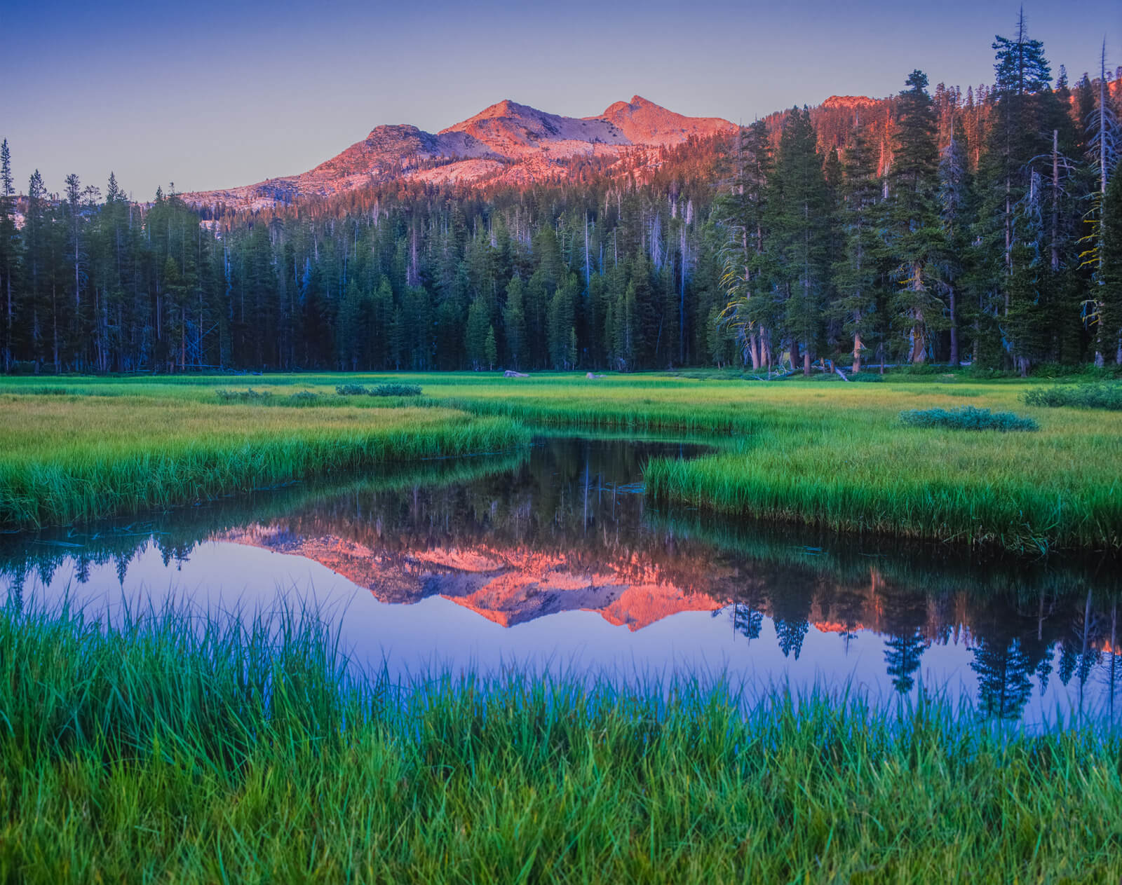 Lake Tahoe at sunrise with mountains bathed in pink light reflected in the still water of the lake